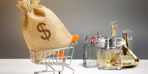 Montagem com um carrinho de compras com um pacote de dinheiro à frente e frascos de perfumes ao fundo