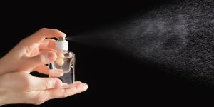 Mãos femininas espirrando um perfume. Fundo preto