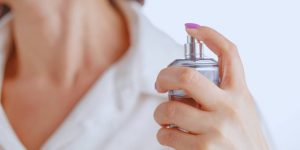 Close na mão de uma mulher espirrando perfume no próprio pescoço