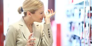 Mulher em uma loja de perfumes segurando um frasco e cheirando o próprio pulso