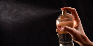 Uma mão feminina aciona o spray de um frasco de perfume sobre um fundo preto