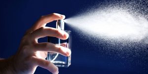 Mão espirrando perfume sobre um fundo azul