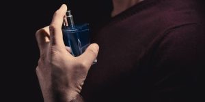 Homem de suéter cor de vinho espirra perfume no próprio pescoço
