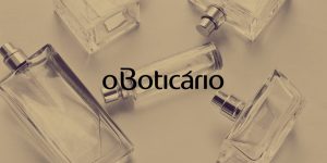 Imagem em tom sépia com frascos de perfume ao fundo e a logo do Boticário centralizada