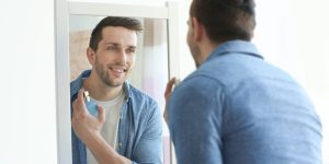 Homem branco se perfumando em frente a um espelho
